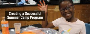 Featured Image of a child smiling and waving at the camera while working on a painting project at summer camp