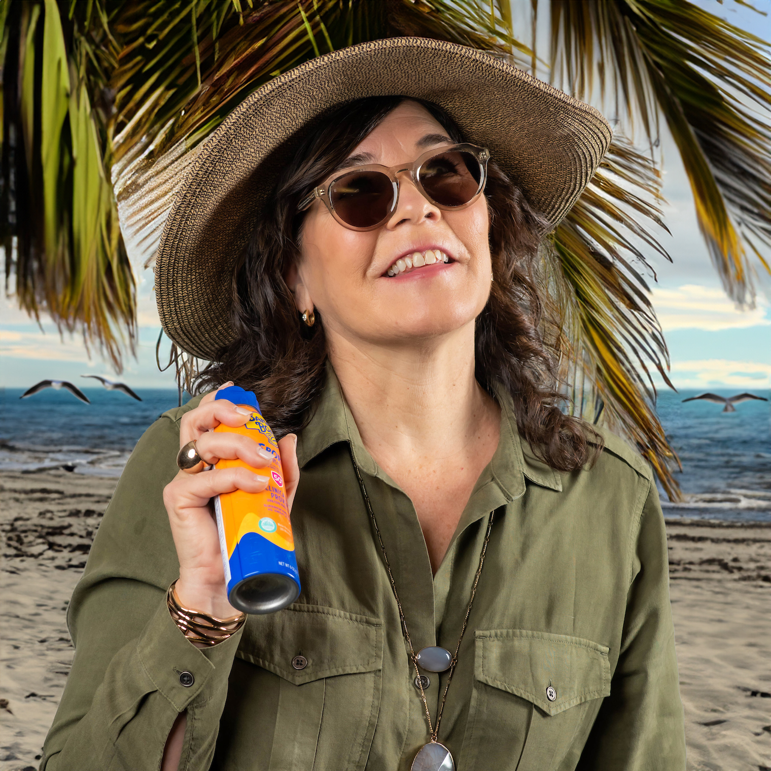 Anette Airy fun photo posing with a sunscreen bottle and straw hat with a beach background