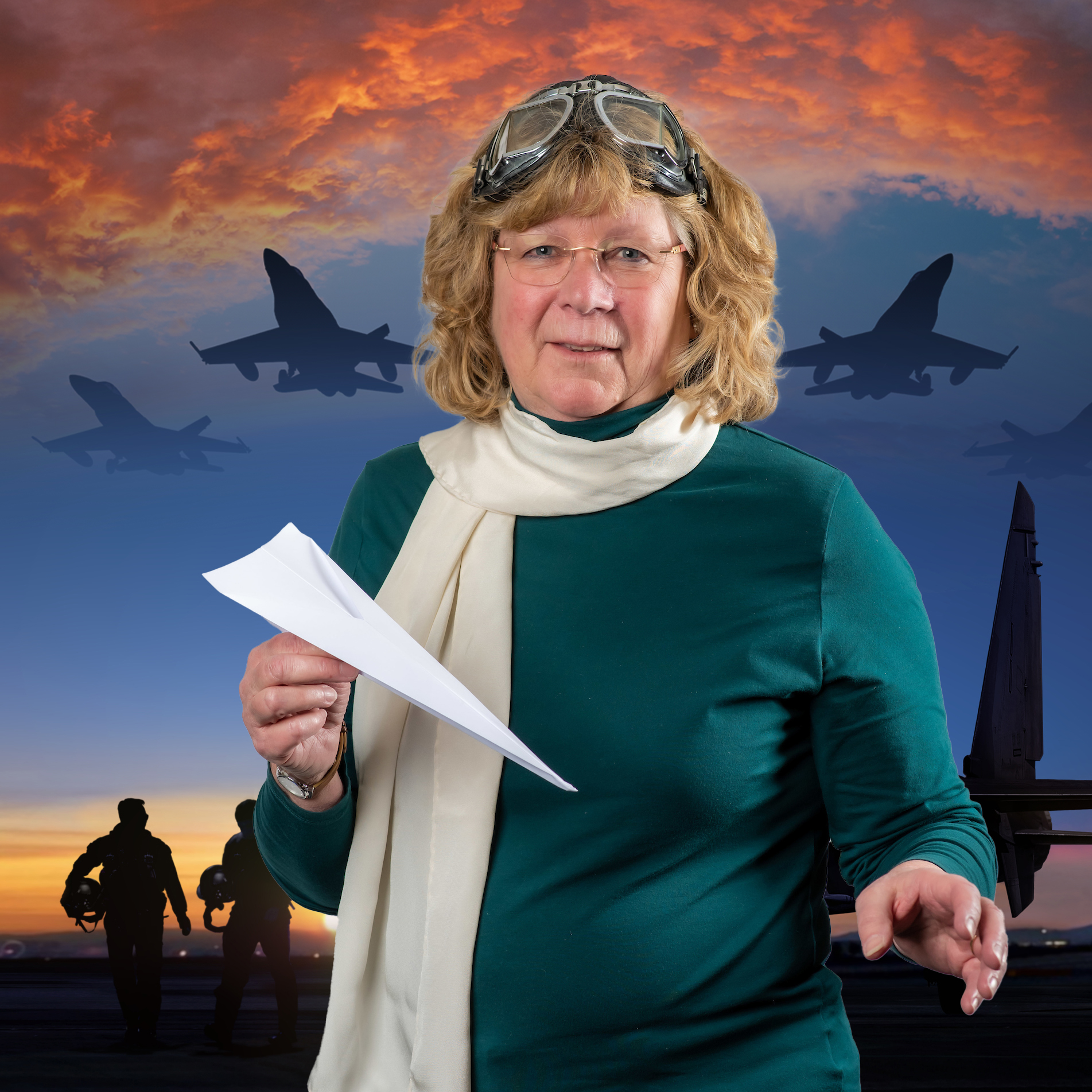 Terri Lewis posing iwth a paper airplane and scarf with jets flying at dusk in the background