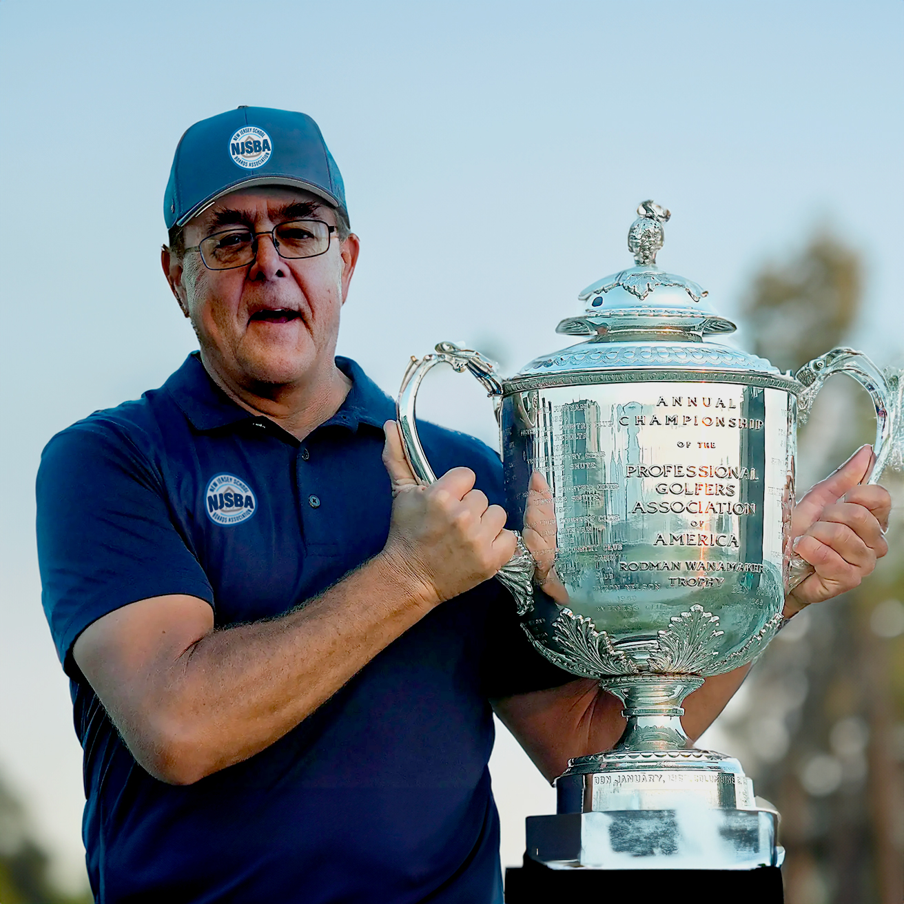 Charlie Muller fun photo wearing an NJSBA polo and hat holding up the Rodman Wanamaker Trophy