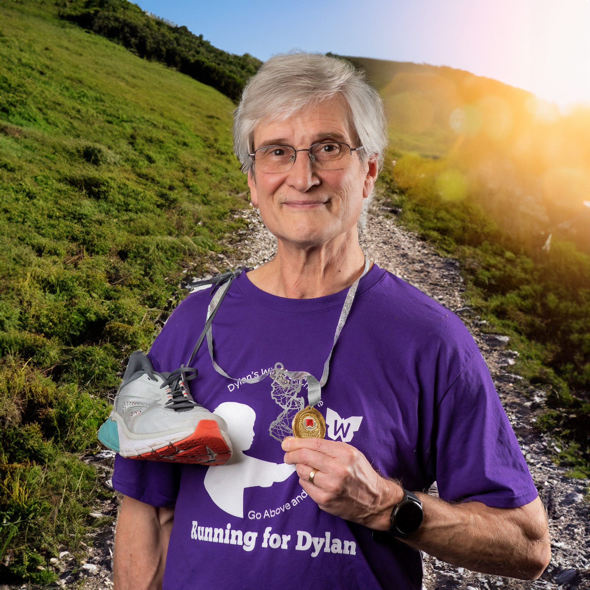 Ray Pinney posing with running shoes around his neck holding a medal, with a hiking trail in the background