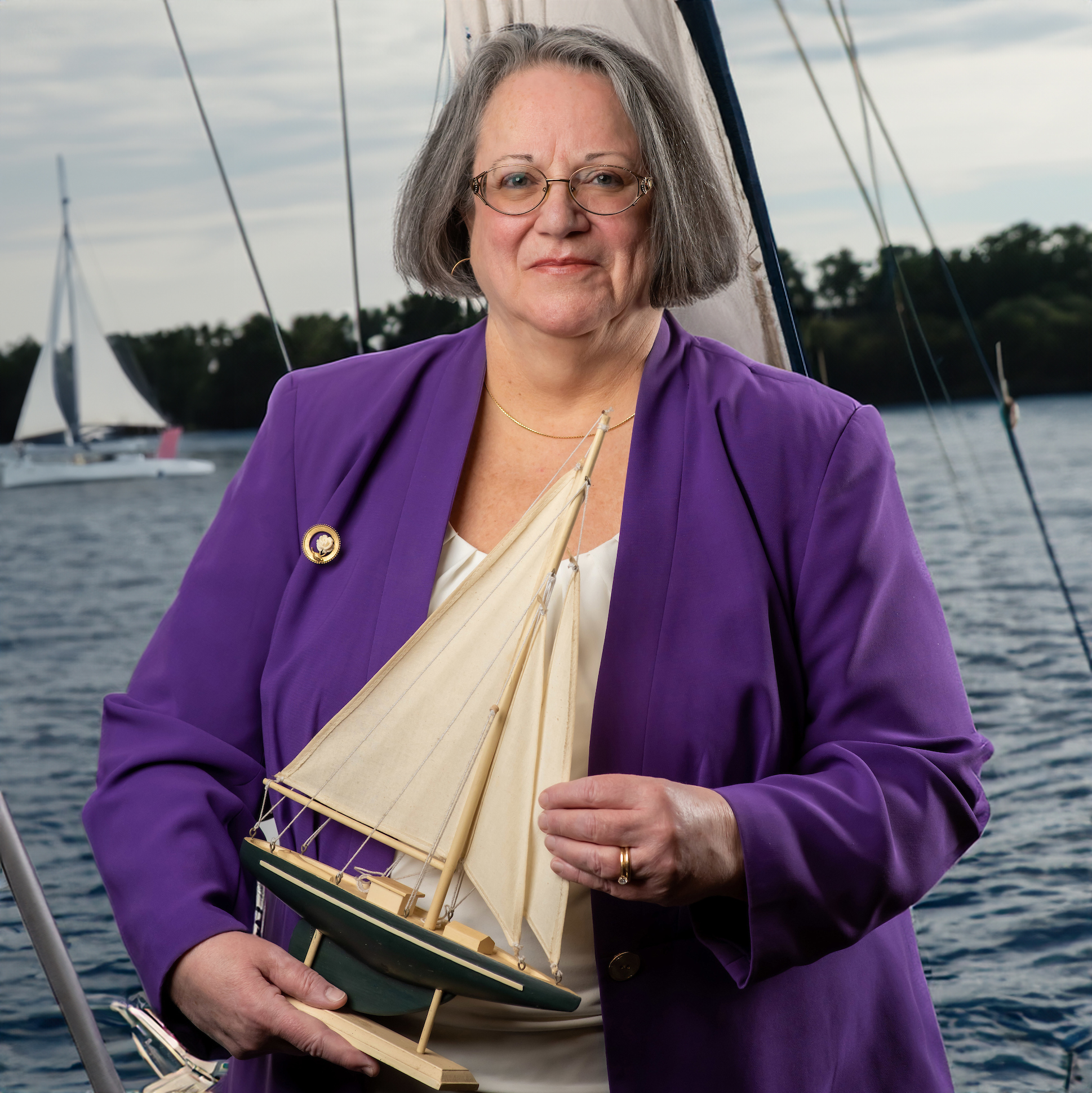 Ann Marie Smith fun photo posing with a model sail boat with a lake and sail boats in the background