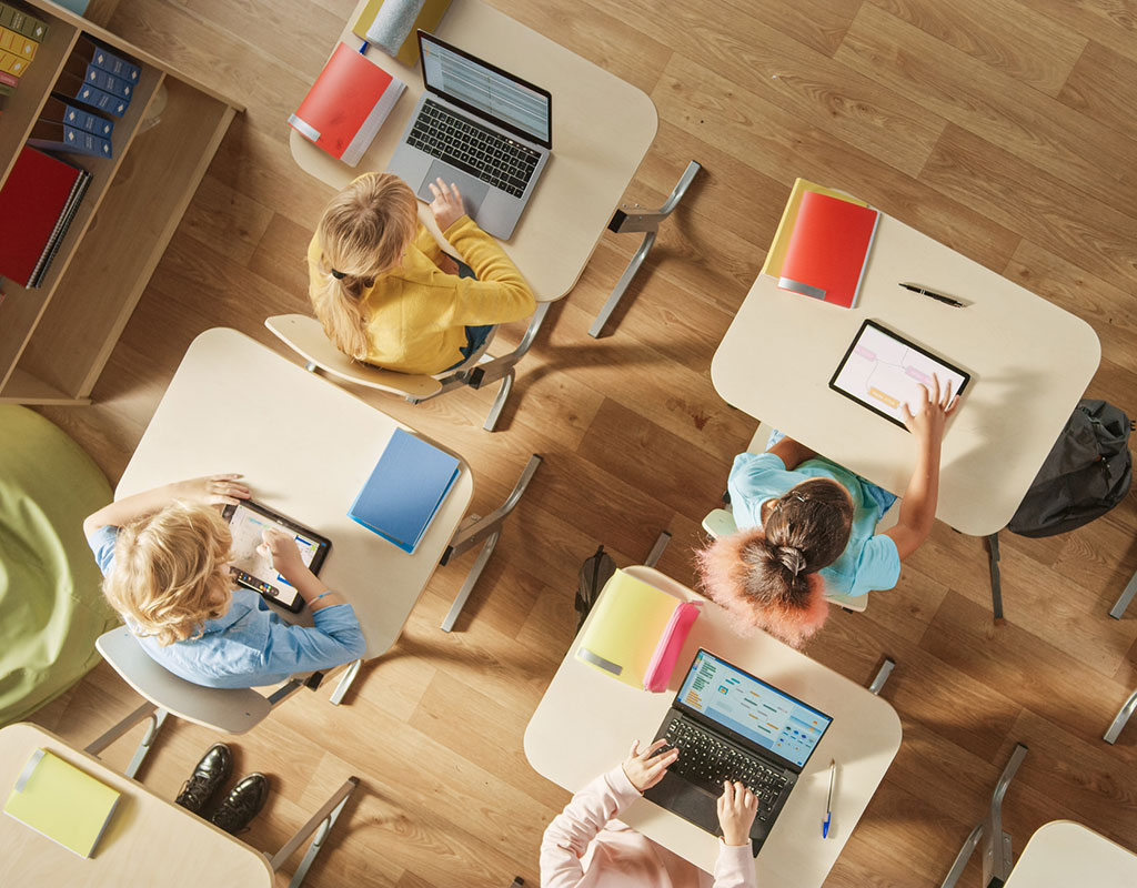 Birdseye view of students sitting at desks using tablets and laptops in the classroom