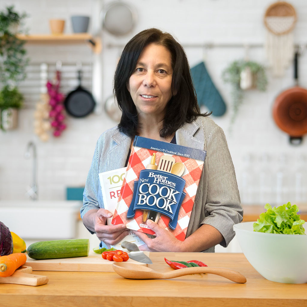 Annette Goddard standing in a kitchen holding cookbooks