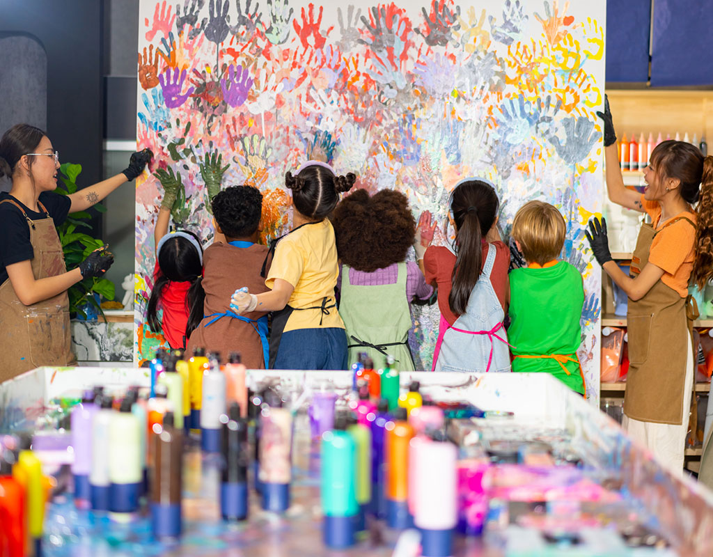 group of diverse kids painting colorful hand prints on a wall