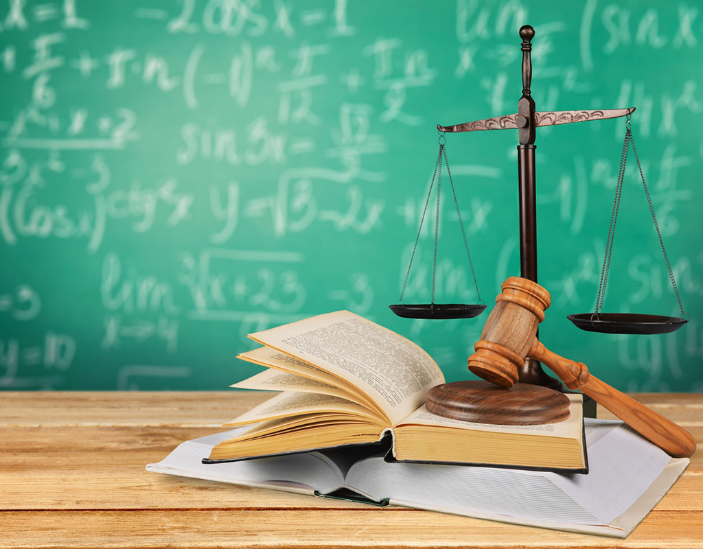 Books, a gavel and the scales of justice sitting on a desk in front of a chalkboard