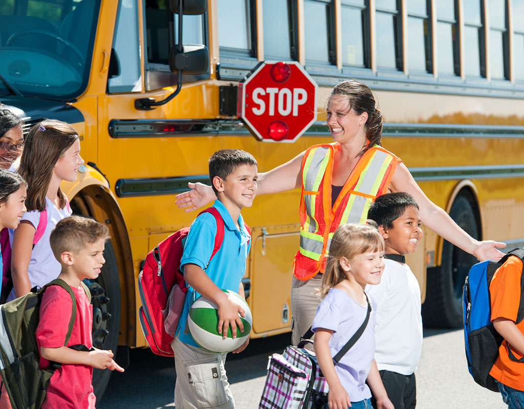 Crossing guard helping students getting off a bus with the stop sign extended 