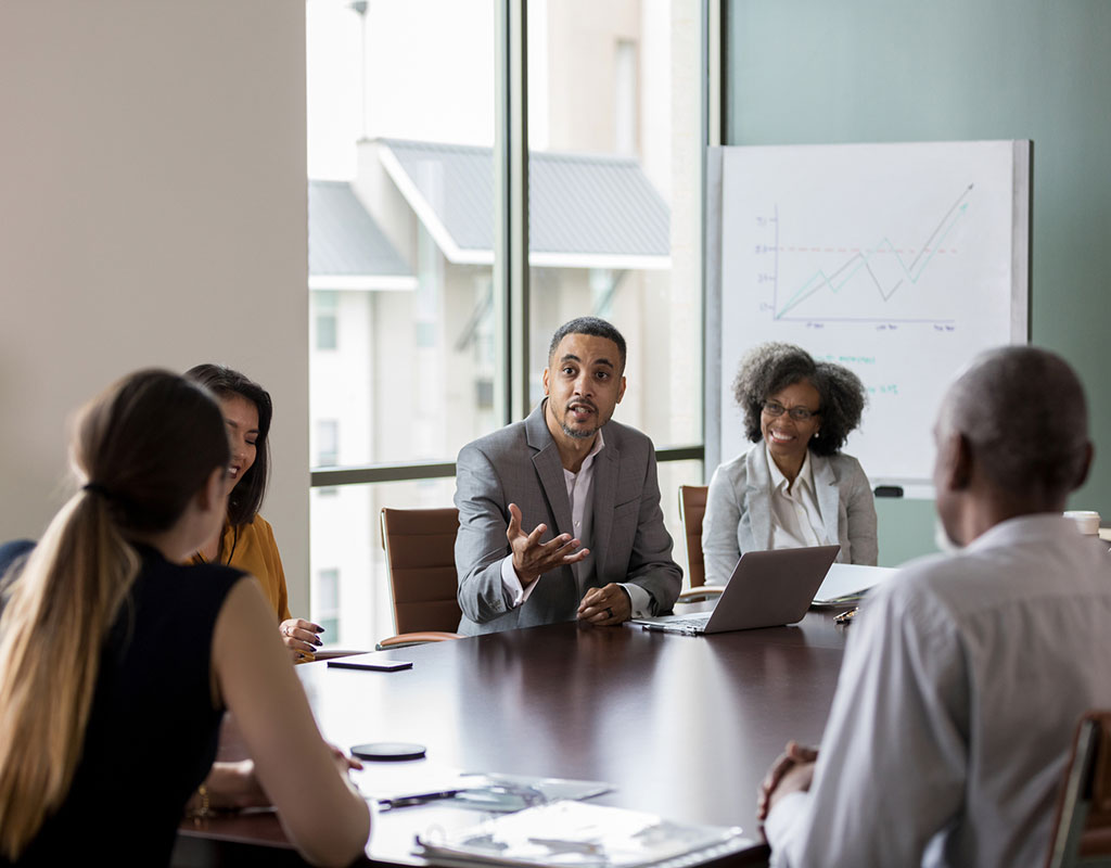 Mid adult businessman gestures as he discusses sales with a group of colleagues during a meeting.