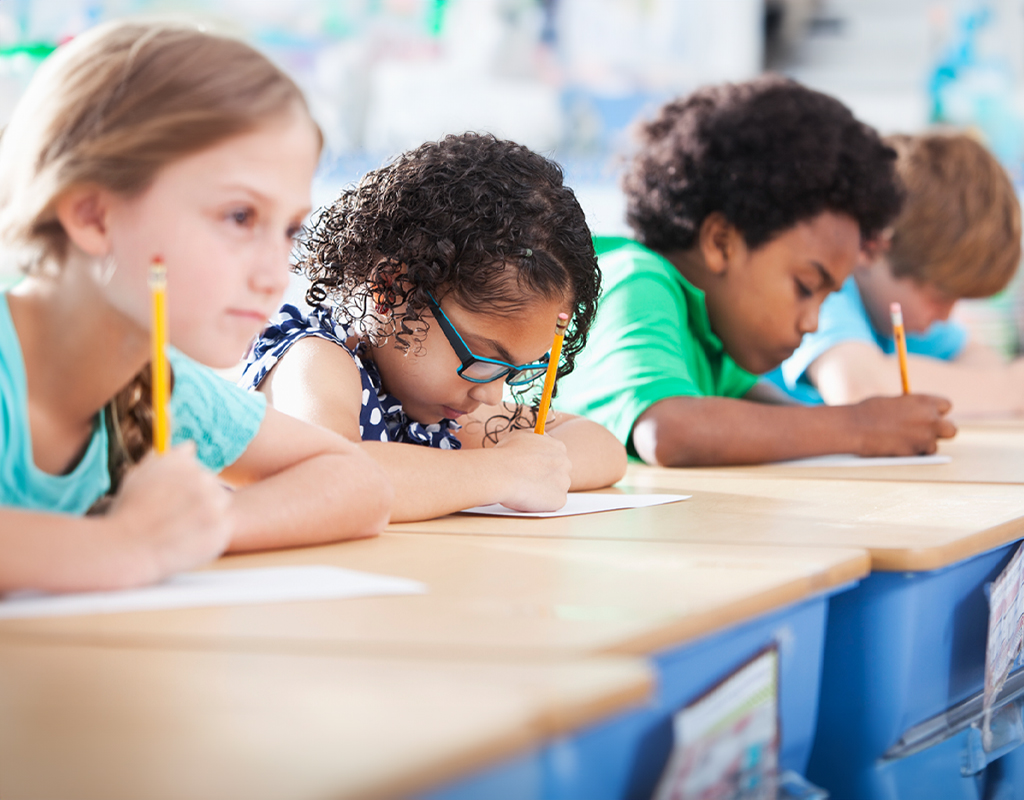 Diverse student sitting at desks in a line with pencils in hand