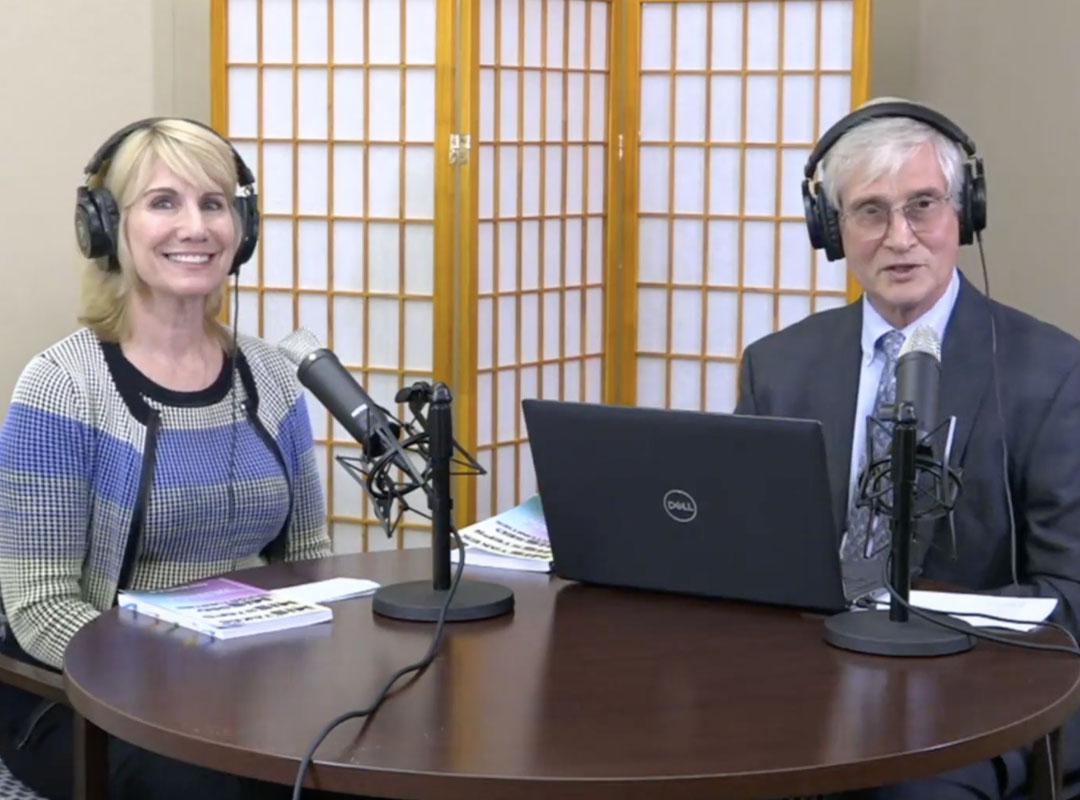 Ray Pinney and Tracey Severns sitting at a table with microphones during their podcast